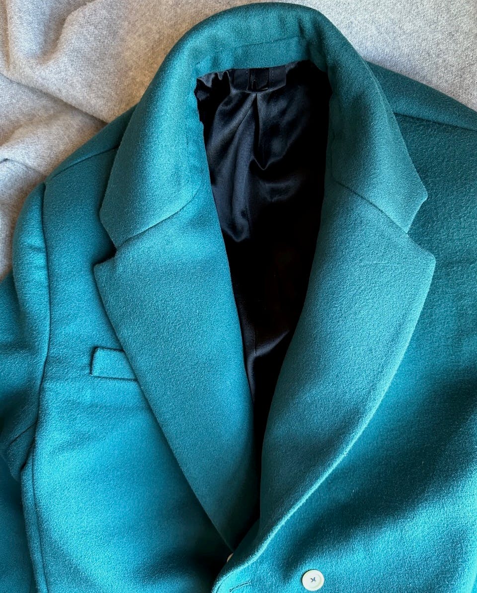 Flat lay of the top half of the coat showing to show the seamlines around the collar, notched lapel and the shiny black lining