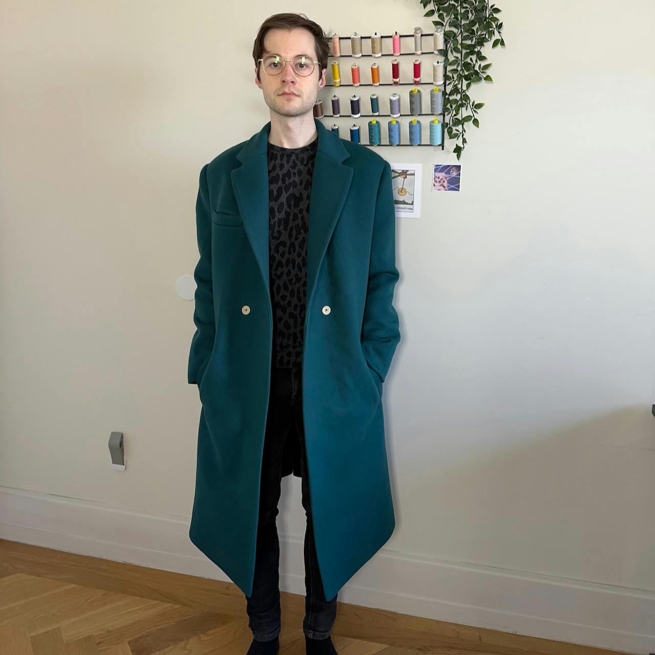 Me standing facing the camera straight-on wearing a structure blue-green wool coat with strong shoulders and a notched lapel. The float arches out from the waist down to the hem reaching my knees due to wearing it unbuttoned.